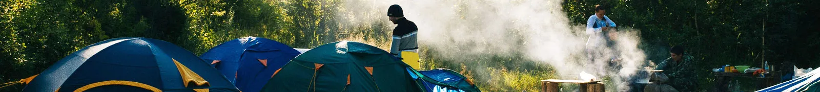 Tents and campers by a smoking campfire in the countryside